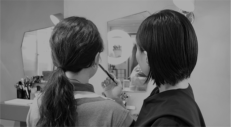 A makeup instructor demonstrating makeup techniques in front of a mirror to a student