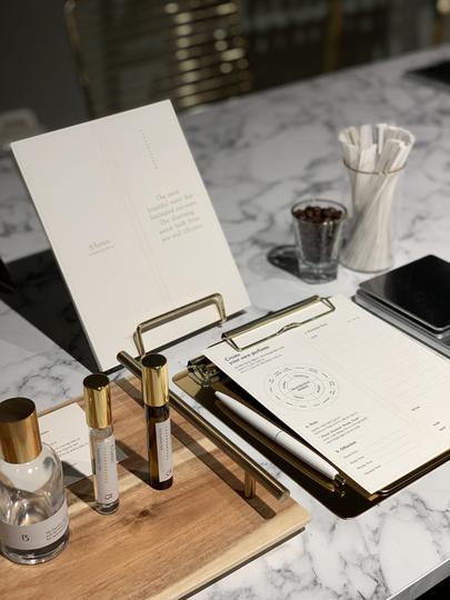 A workshop where perfume sample bottles, notebooks, and pens are placed on a marble desk, with tools for the perfume-making process neatly arranged