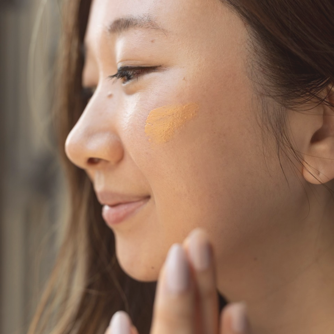 A woman applying yellow sunscreen to her face