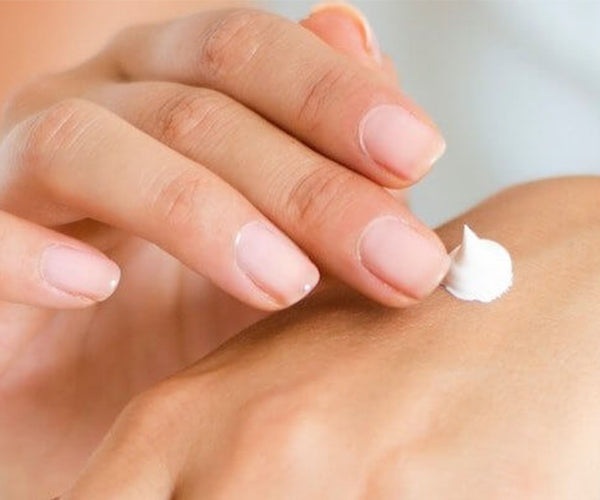 A skincare cream product in a white color spread thinly on the fingertips