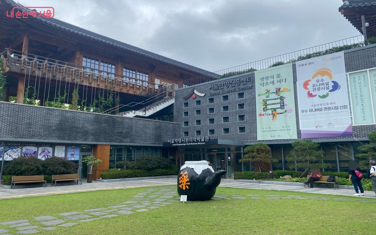 A view of the garden of the Korean medicine promotion center, with a large black jar-shaped sculpture and a lawn