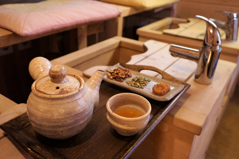 Inside a hanok cafe, a table with a wooden foot-bath container and a traditional tea set