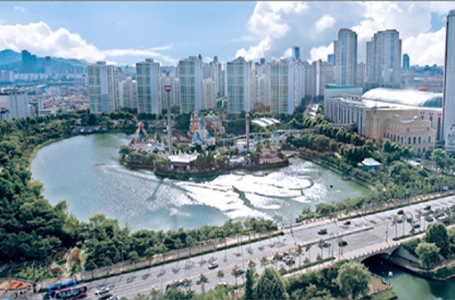 A panoramic view of Seokchon Lake, surrounded by a walking path and trees along the water's edge.