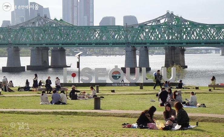 This shows visitors relaxing on the lawn plaza of Nodeul Island with Hangang Bridge in the background..