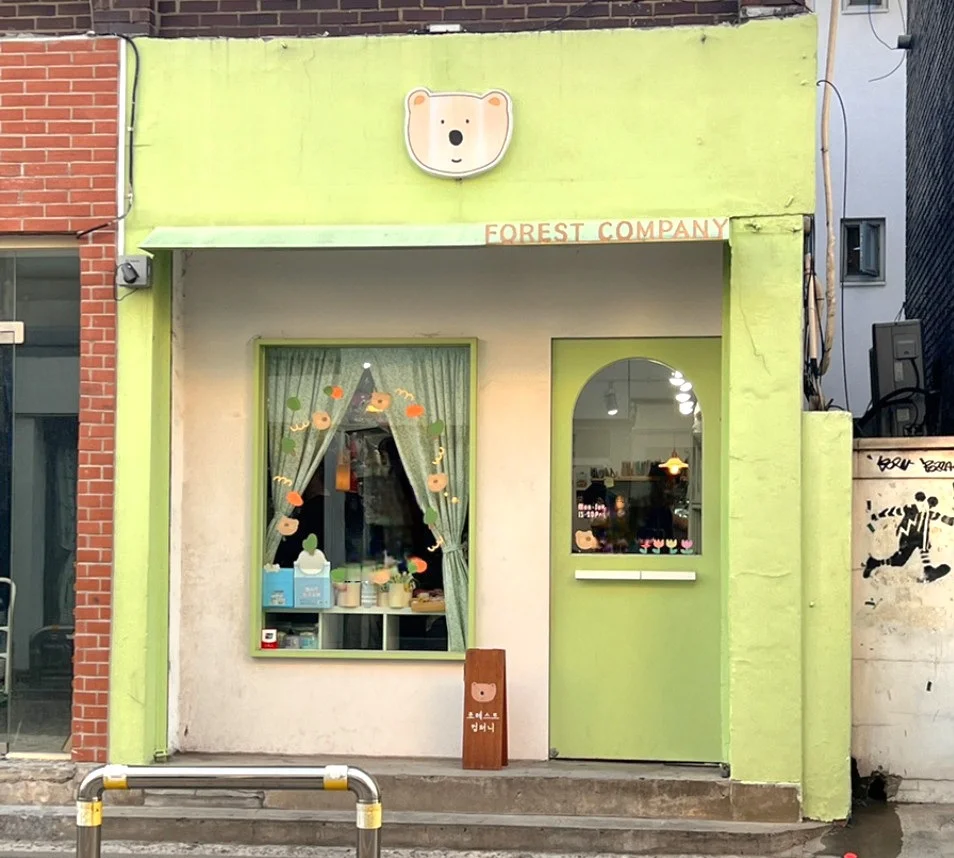 This is a street scene showing the front of a small shop and a light green exterior wall on Mangnidan-gil..