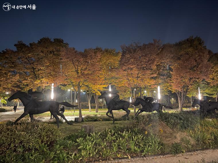 조명이 켜진 밤의 서울숲 군마상과 가을 수목을 담은 사진이다.